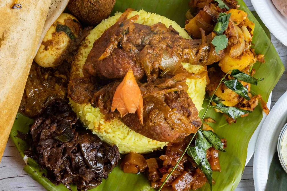 Yellow ghee rice with chicken curry, egg, frikkadel and sambols on banana leaf